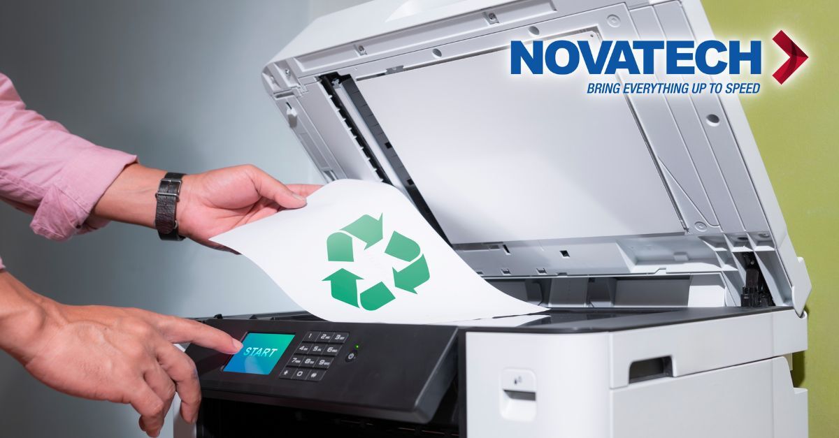 A person loads a sheet of paper featuring a recycling symbol into a multifunction printer and presses the