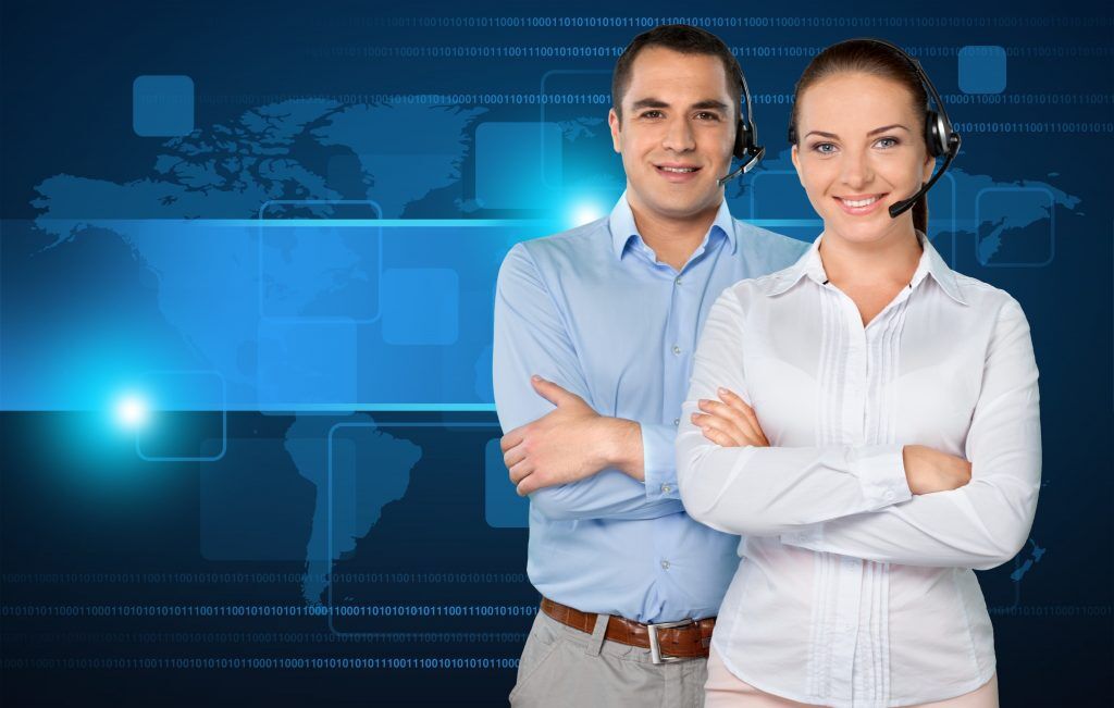 Two smiling call center agents, a man and a woman, wearing headsets and standing with their arms crossed, are depicted