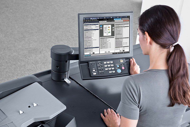A woman operates a large office machine with a touchscreen interface and a keypad.
