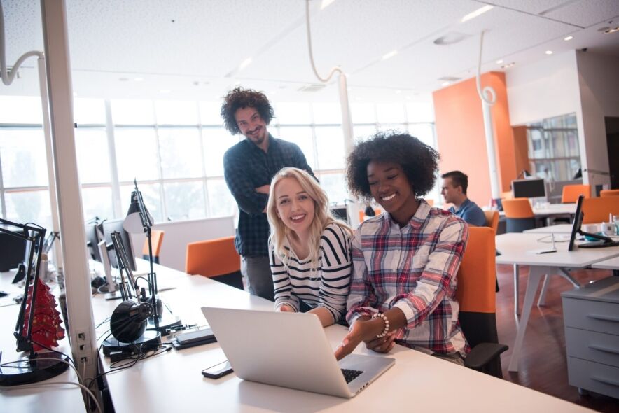 Three colleagues are collaborating on a laptop in a bright, modern office.
