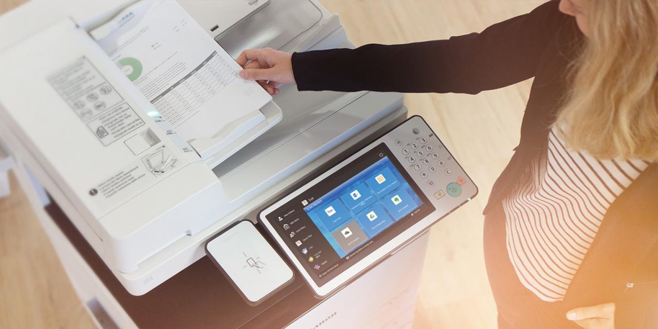 A woman is placing a document into a copier's document feeder.