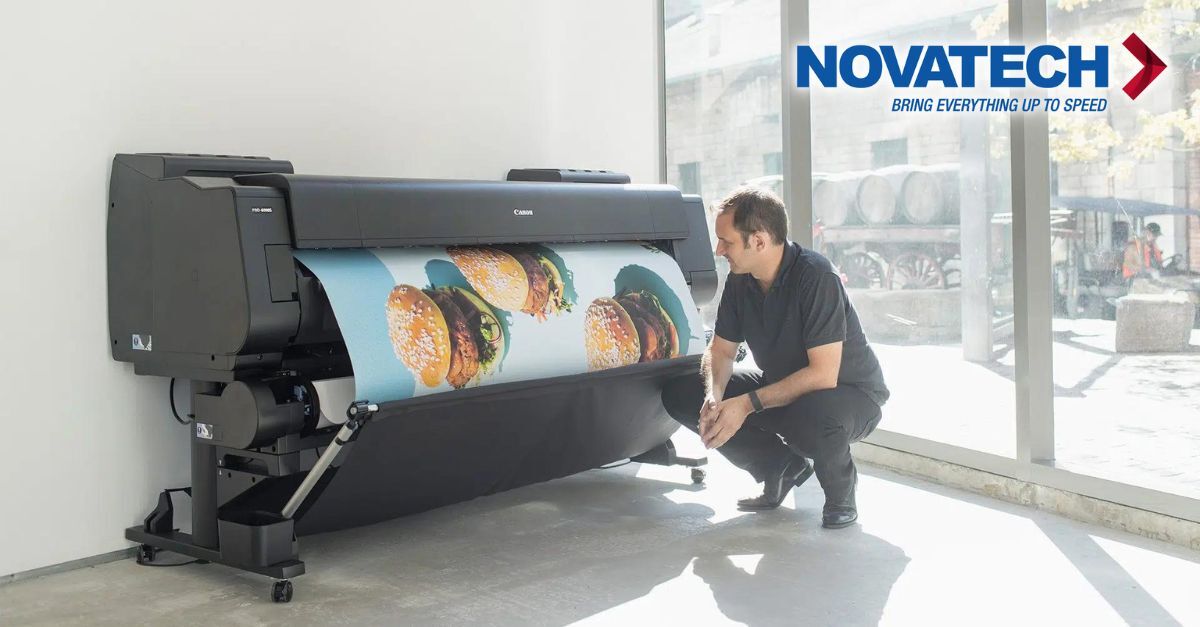 A man observes a large Canon printer producing a vibrant print of hamburgers, situated in a bright room with a Novatech