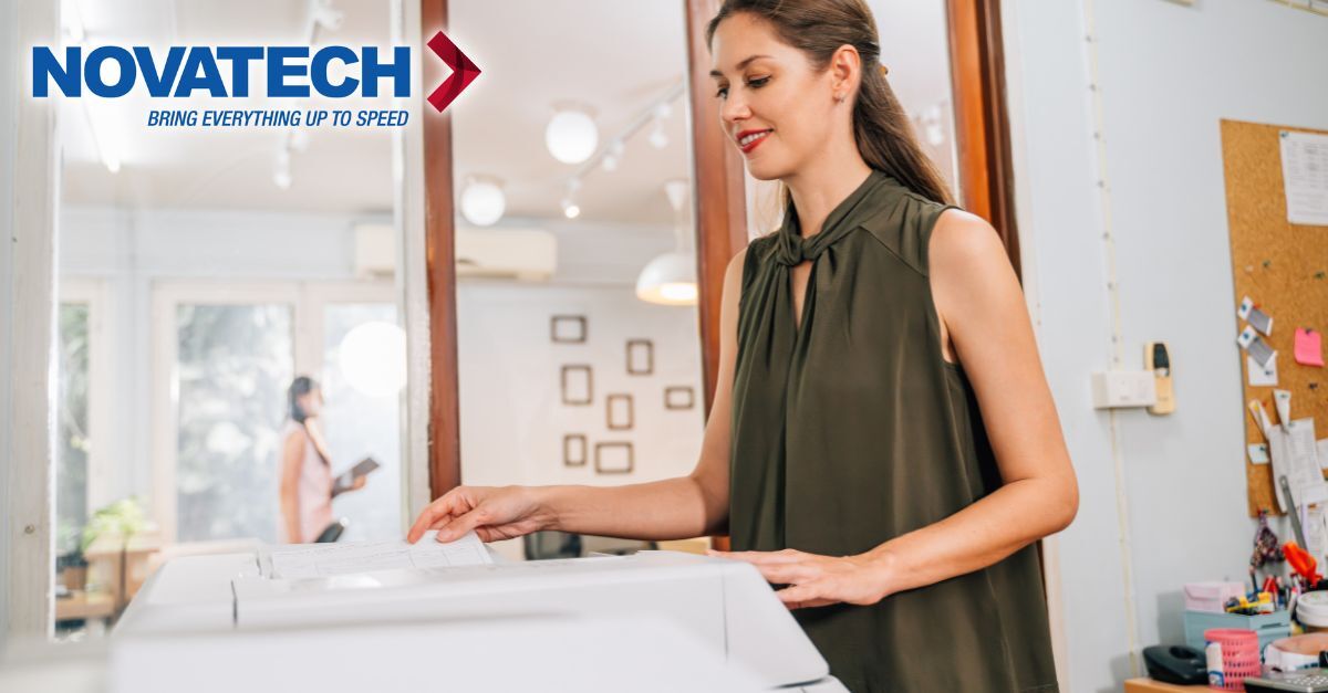 A woman in a green sleeveless top is operating a copier in an office environment, with the