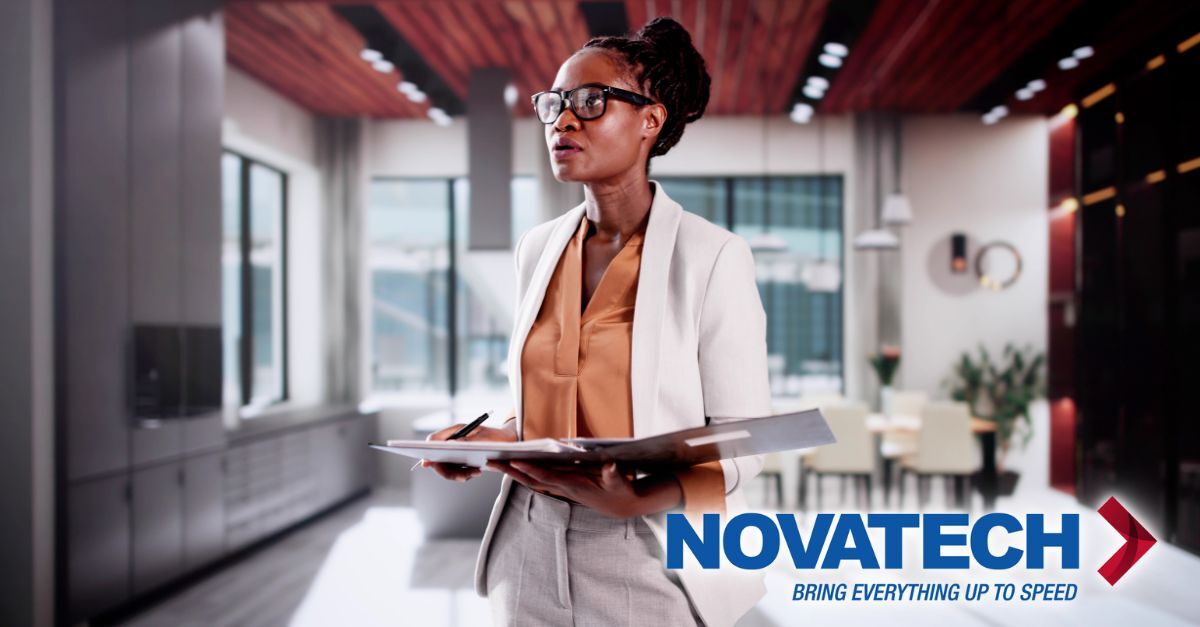 A businesswoman in a white blazer and glasses holds a folder while standing in a modern office with a logo that reads