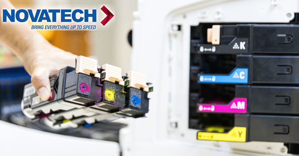 A hand holds several colorful toner cartridges in front of a printer's ink cartridge slots, with the Novatech logo