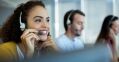 A smiling woman wearing a headset is talking on the phone in a call center.