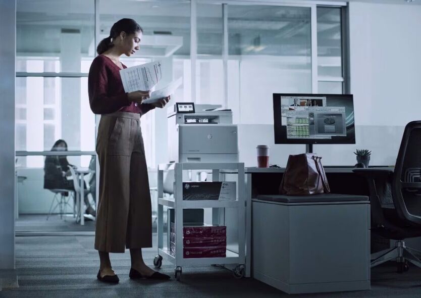A person's hand interacts with a digital security icon while another person reviews documents in an office setting.