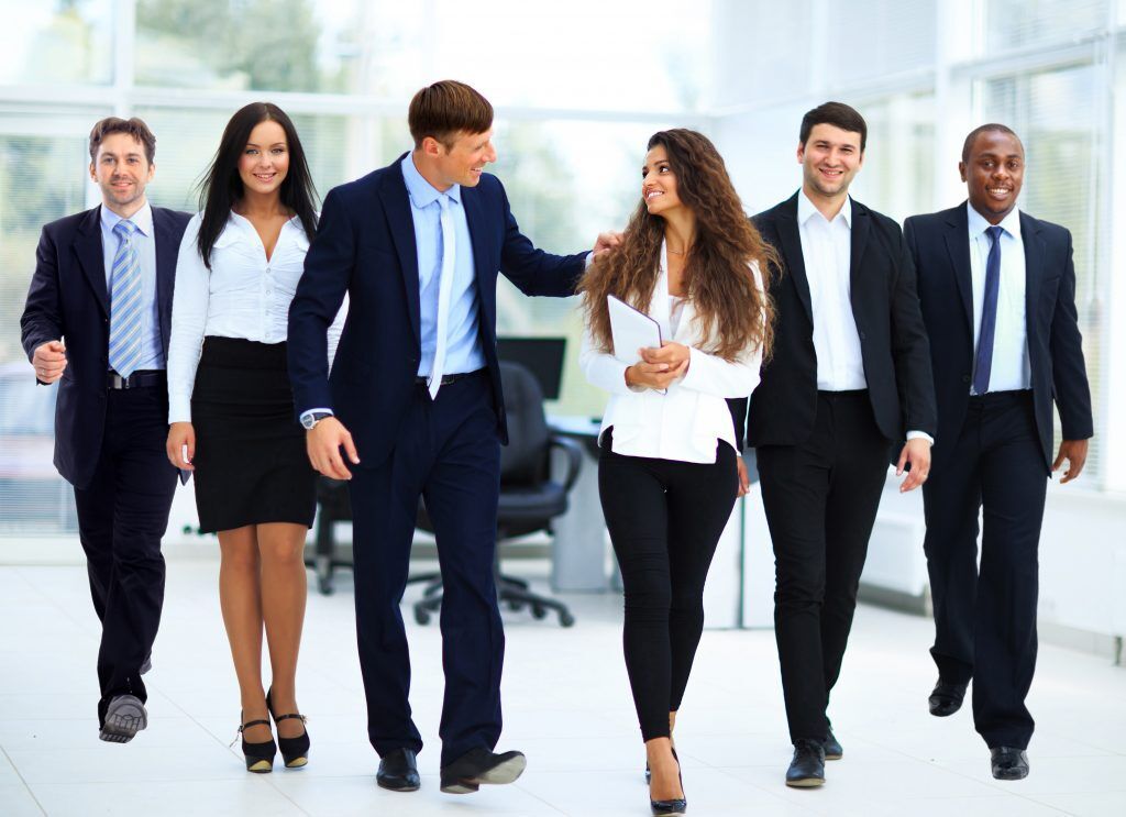 A diverse group of business professionals walks together in an office environment.