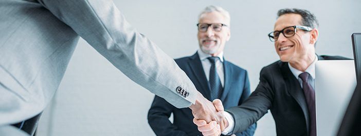 Three businessmen in suits shake hands in a professional setting.