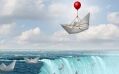 A single paper boat, lifted by a red balloon, hovers above a waterfall while other paper boats sail towards the edge.
