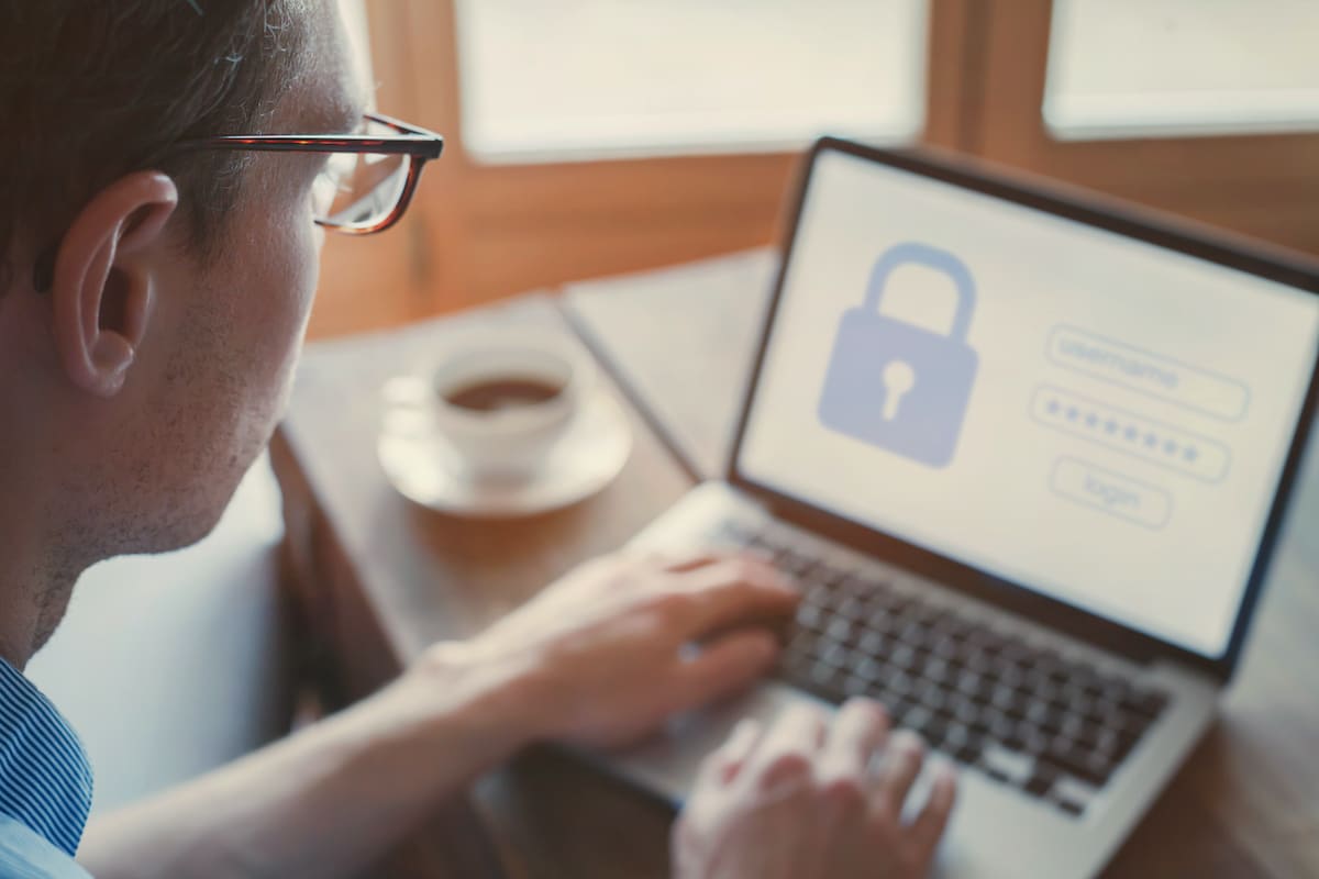 A person wearing glasses types on a laptop displaying a login screen with a padlock icon.