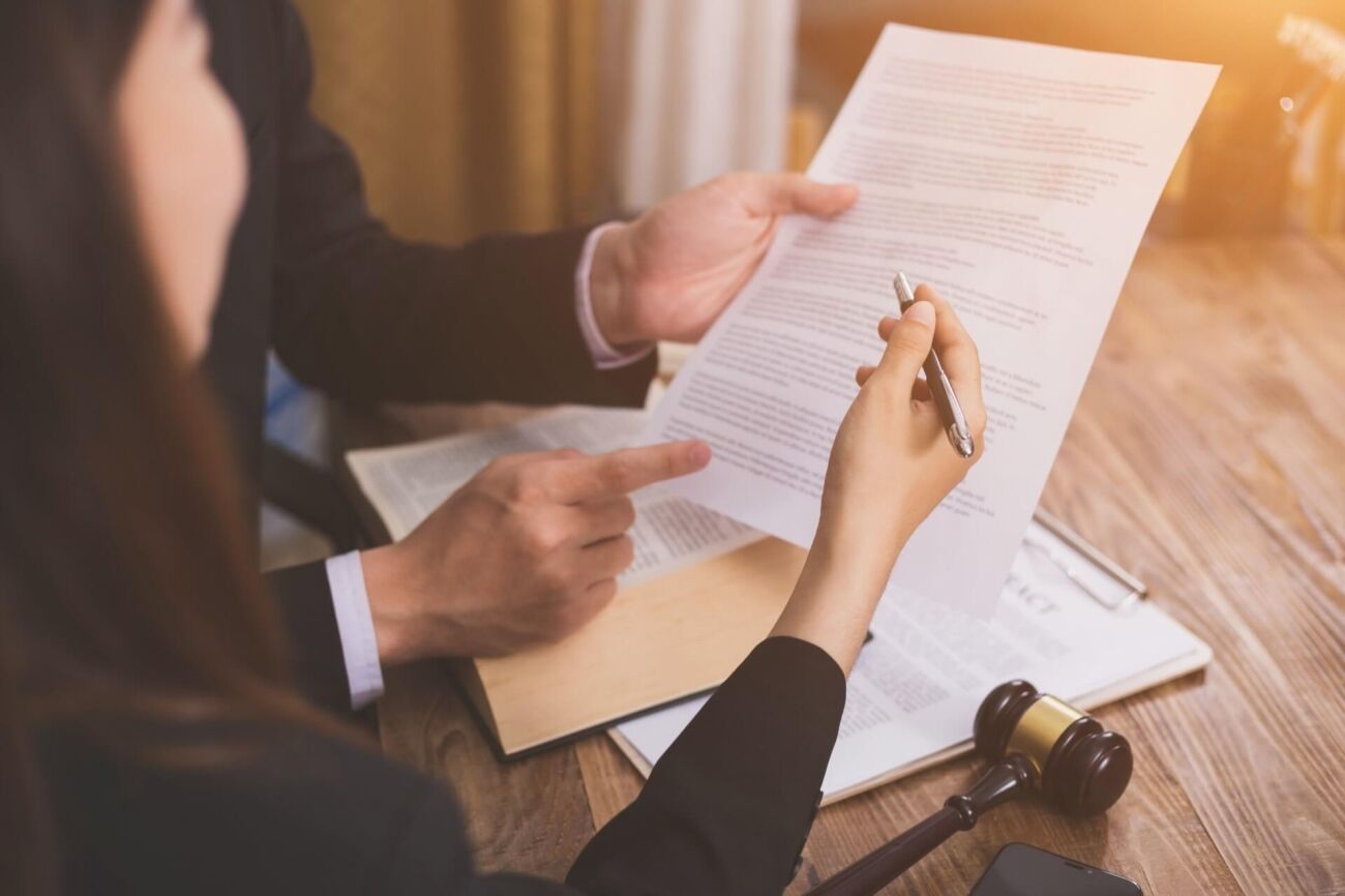 Two people in suits are reviewing legal documents at a wooden desk, with a gavel and a smartphone nearby.