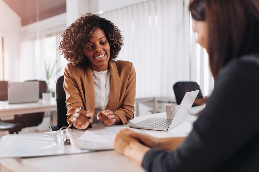 Two women are in a professional meeting, with one reviewing documents and the other looking on.
