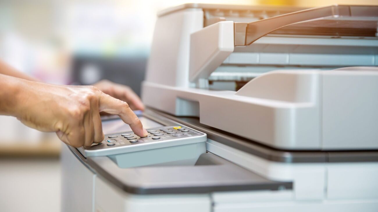 A person's hand is pressing buttons on the control panel of a copier.