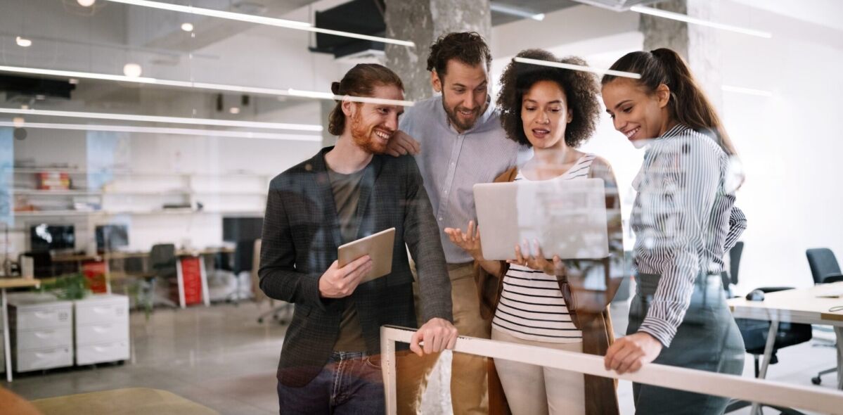 Four colleagues collaborate on a laptop in a modern office setting.