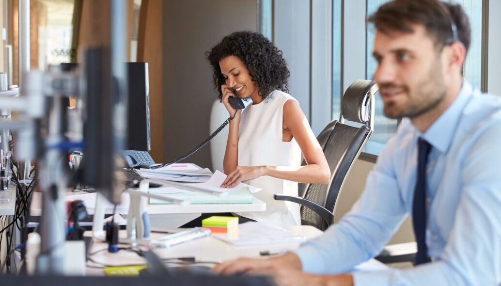 A woman on the phone and a man at his computer work in a modern office environment.