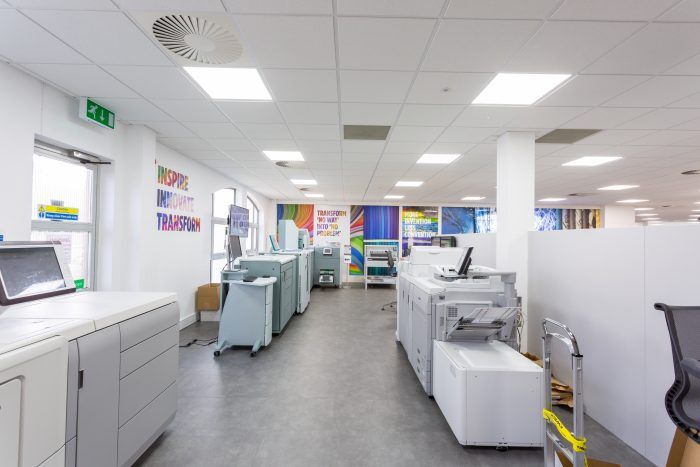 A modern printing facility is depicted, showcasing rows of large-scale printing machines and a clean, well-lit