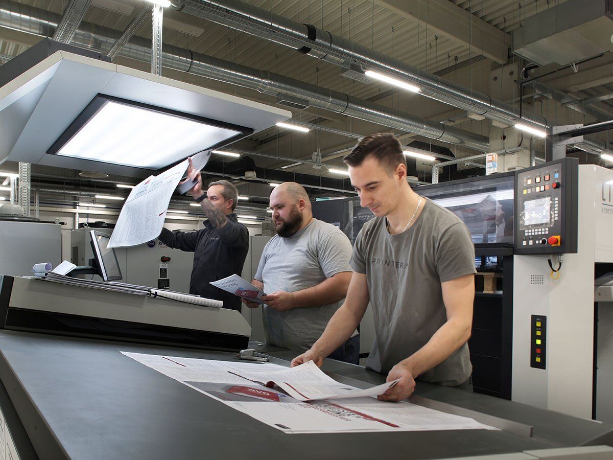 Three men are working in a printing facility, inspecting printed materials.