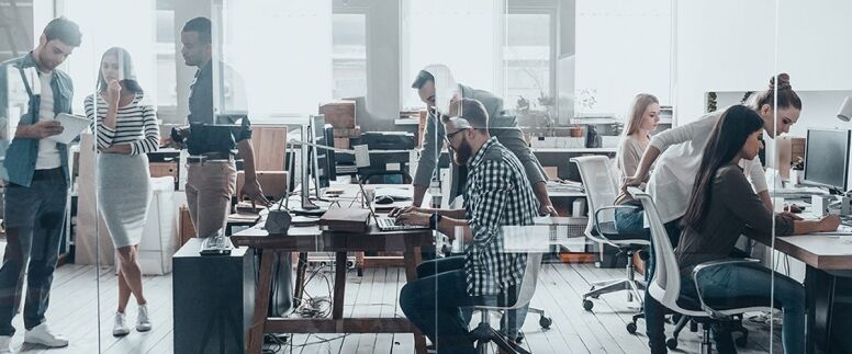 A group of diverse colleagues collaborate and work on projects in a modern, open-plan office environment.