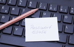A pencil rests on a keyboard next to a sticky note with the handwritten password 