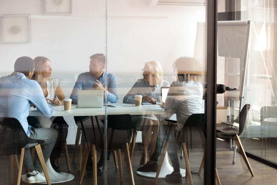 A diverse group of business professionals are gathered around a table in a modern office meeting room, engaged in