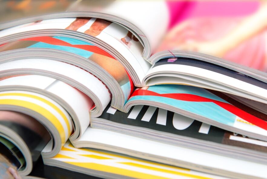A stack of open magazines displays colorful pages with abstract designs and partial images of people.