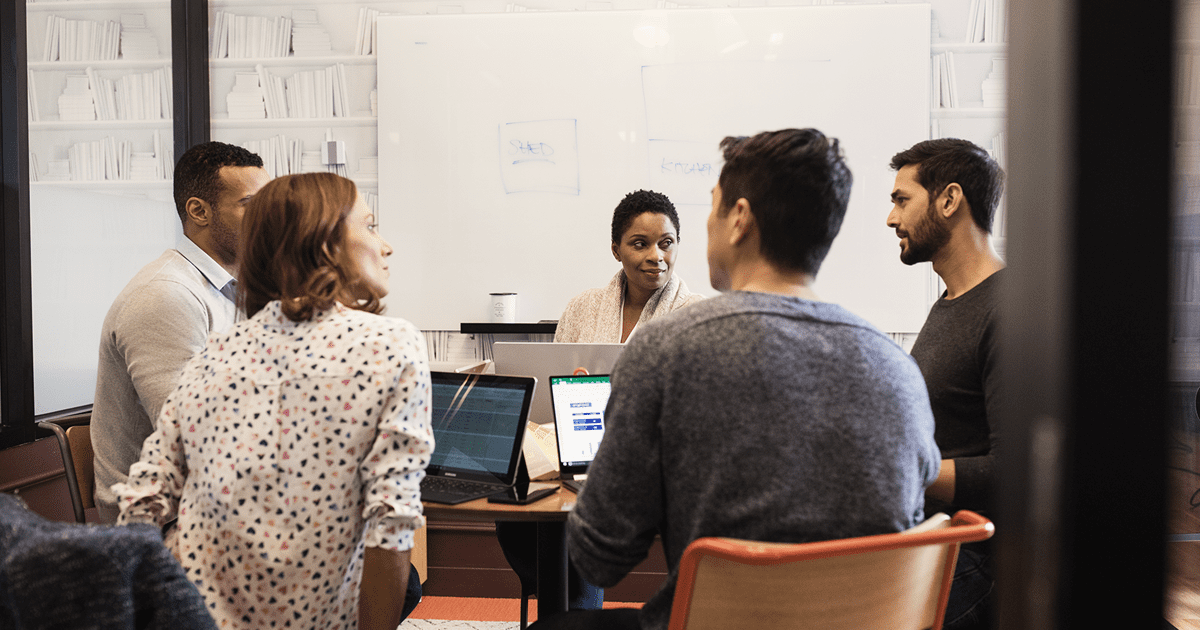 A diverse group of colleagues collaborates around a table with laptops in a modern office setting.