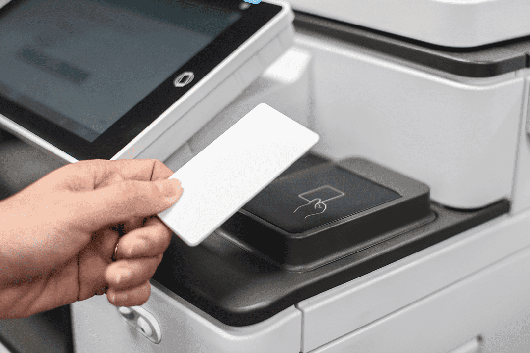 A hand holds a blank white card near a card reader on a white machine.