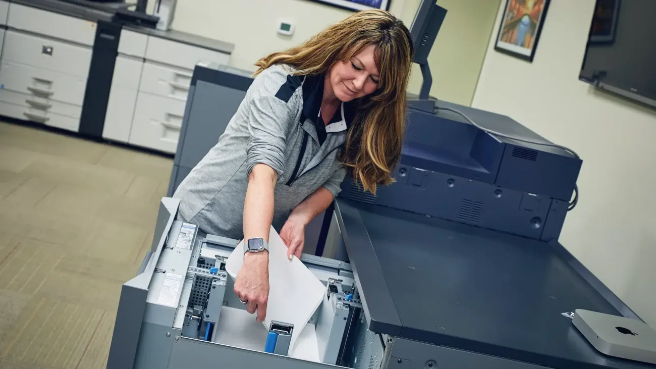 A woman is loading paper into a large printer.