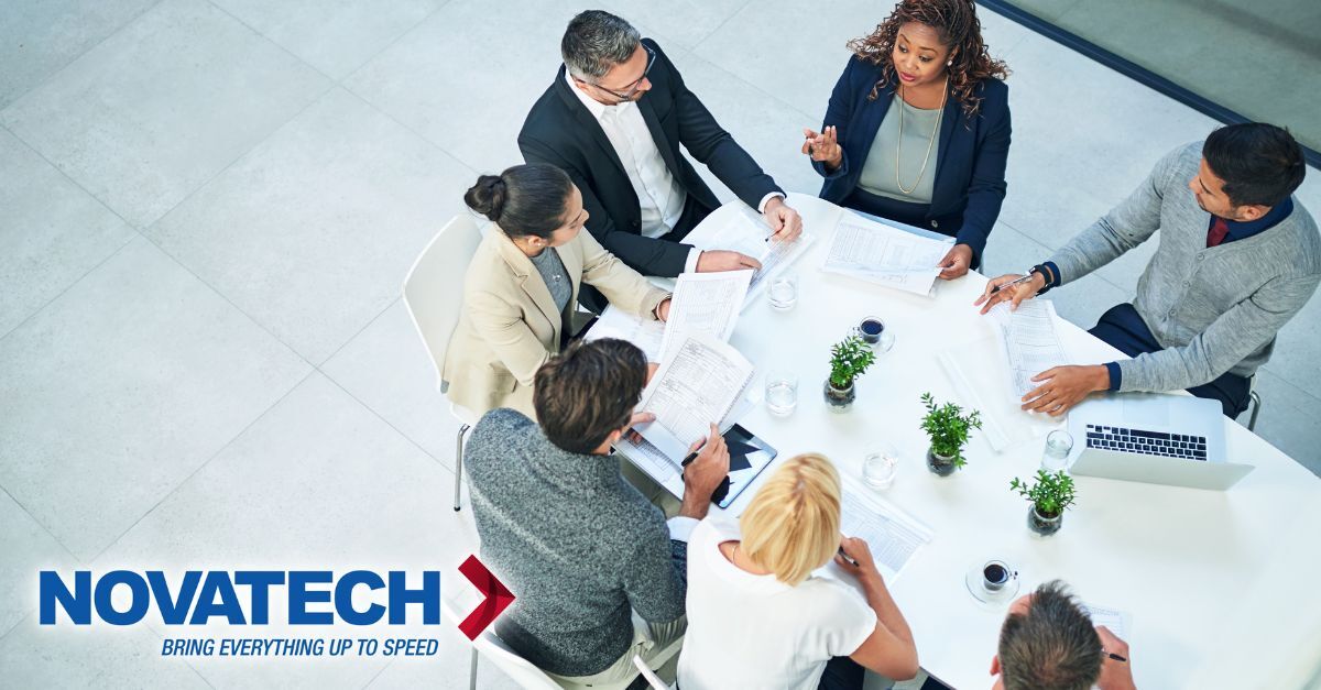 A diverse group of business professionals collaborates around a table, reviewing documents and engaging in discussion.