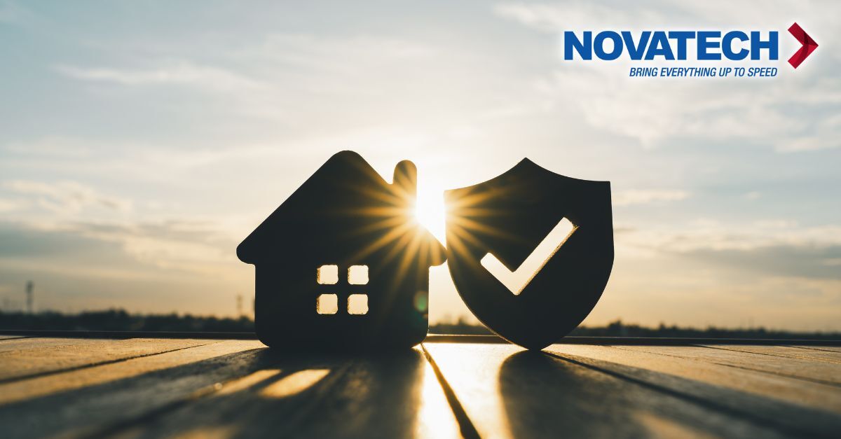 A silhouette of a house and a shield with a checkmark are placed on a wooden surface against a sunset sky, with the