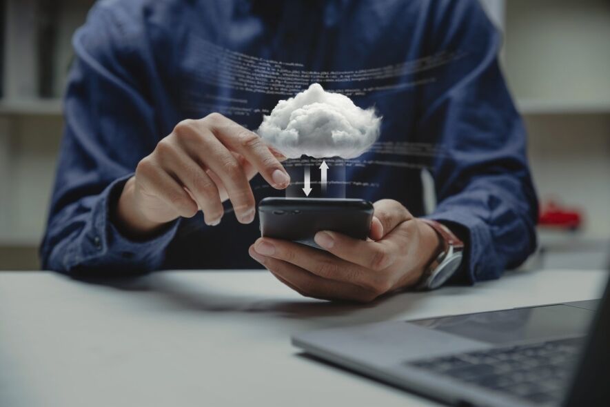 A person uses a smartphone to interact with a cloud computing interface, indicated by the digital cloud and code