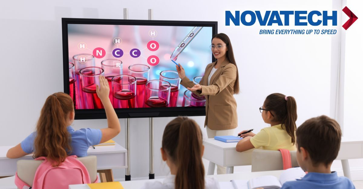 A teacher uses a large interactive screen to teach chemistry to young students in a classroom.