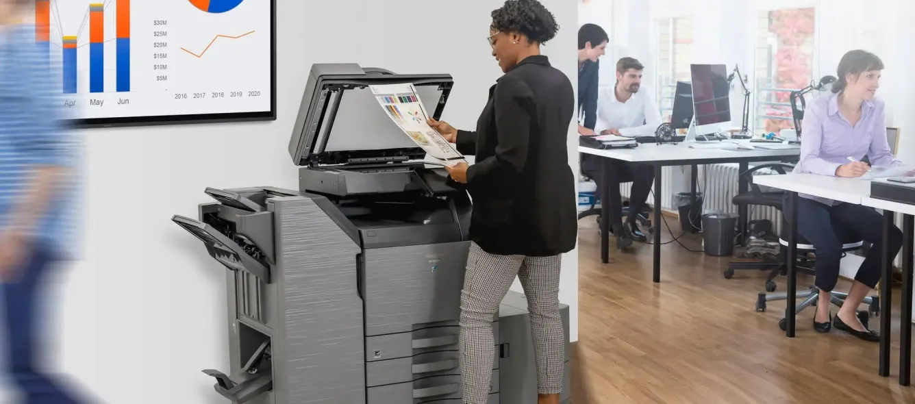 A woman is shown using a copier in an office setting with colleagues working in the background.