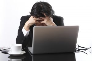 A stressed businessman sits at his desk with his head in his hands, overwhelmed by his work.