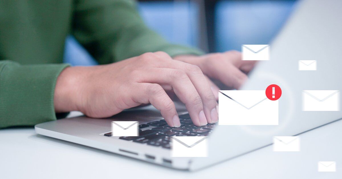 A person's hands are typing on a laptop, with several email icons and one with an exclamation mark overlayed on the