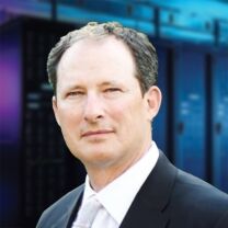 A man in a business suit is featured against a blurred background of server racks in what appears to be a data center.
