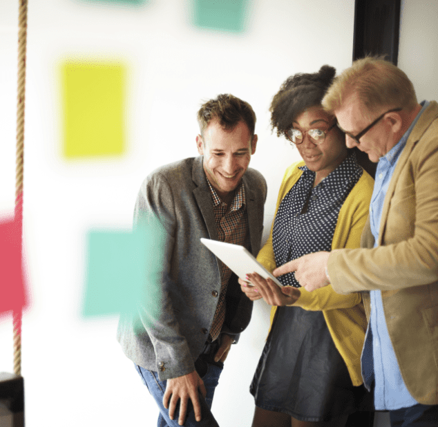 Three colleagues collaborate around a tablet, their expressions suggesting engagement and shared interest in the