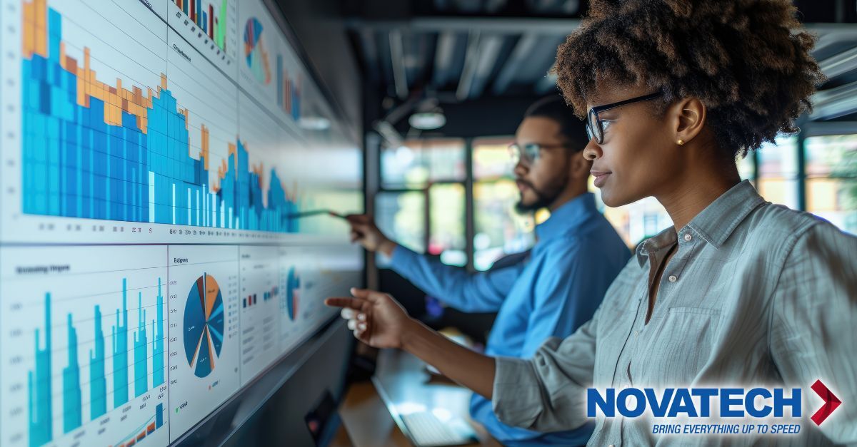 Two business professionals analyze financial data displayed on a large screen, with the Novatech logo prominently