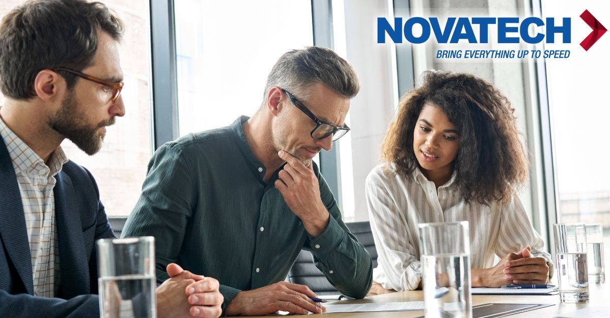 Three professionals are gathered around a table, reviewing documents with a company logo in the background.
