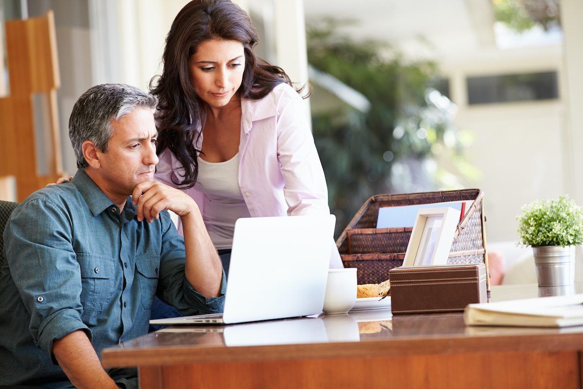 A man and a woman look intently at a laptop screen on a wooden desk.