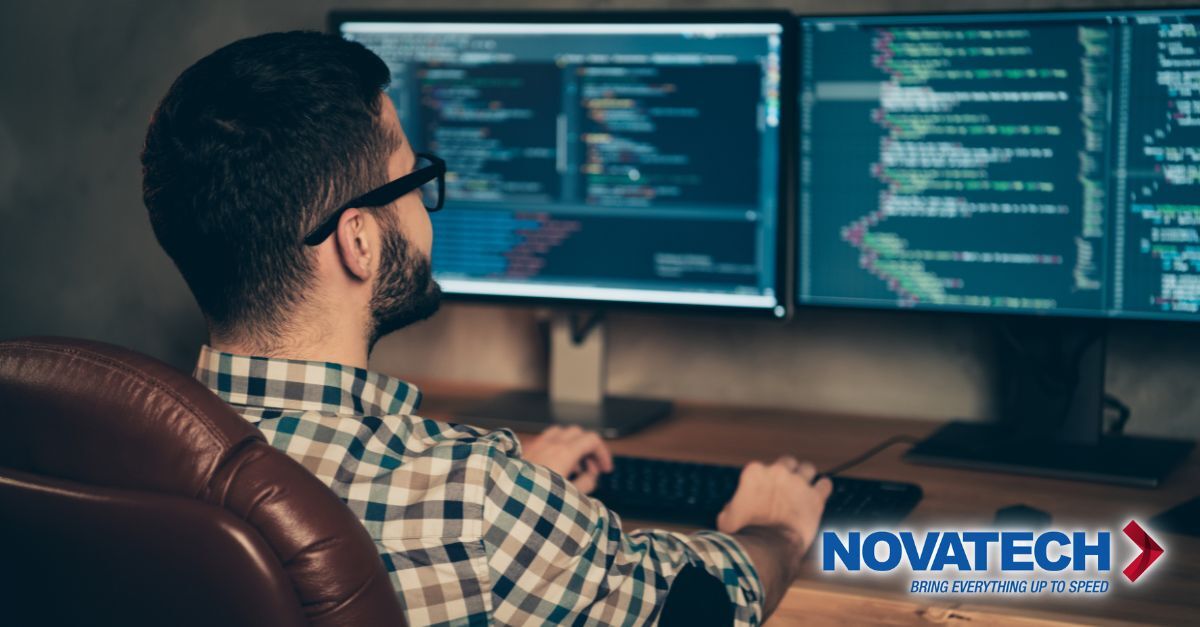 A man with glasses and a plaid shirt is coding on two computer monitors, with the Novatech logo in the lower right