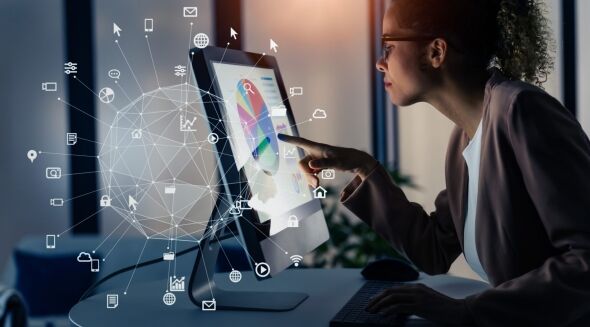 A woman in glasses is interacting with a digital interface displaying a pie chart and network of icons on a computer