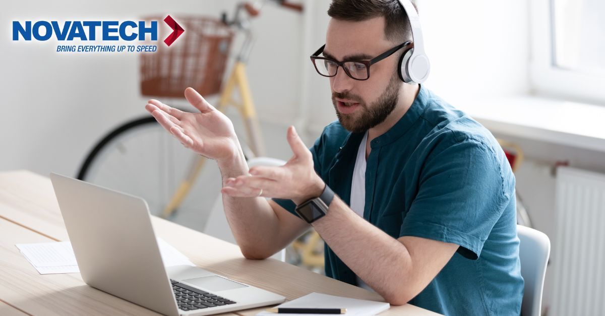 A man wearing headphones and glasses gestures while looking at his laptop during a video call.