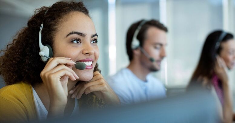 A smiling woman wearing a headset is talking on the phone in a call center.