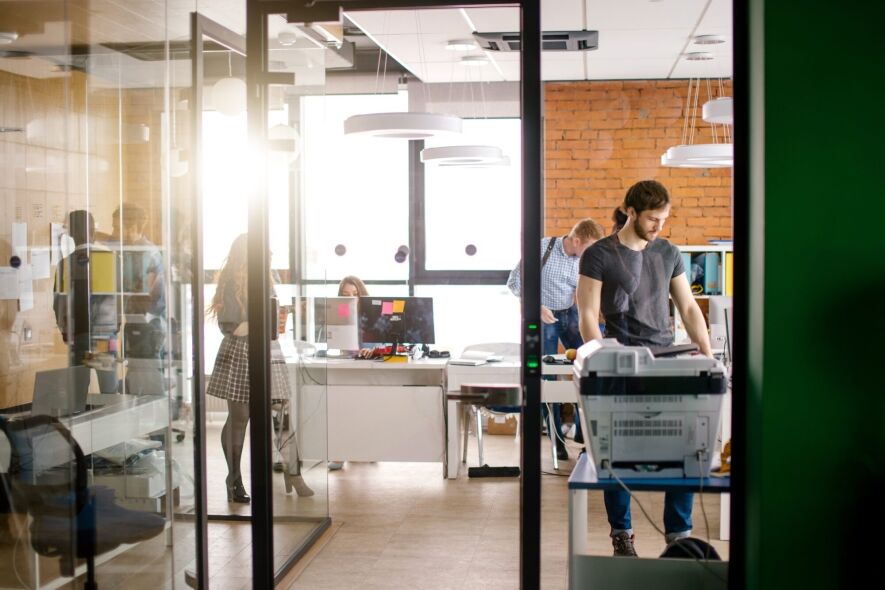 A group of people are working in a modern office with glass walls and bright lighting.
