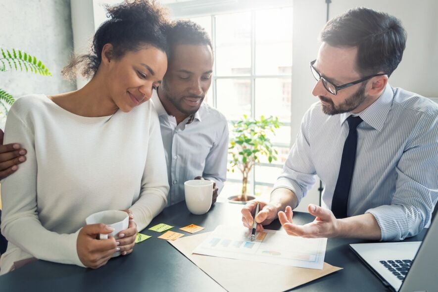 A diverse group of three people are gathered around a table, reviewing documents and charts, suggesting a business
