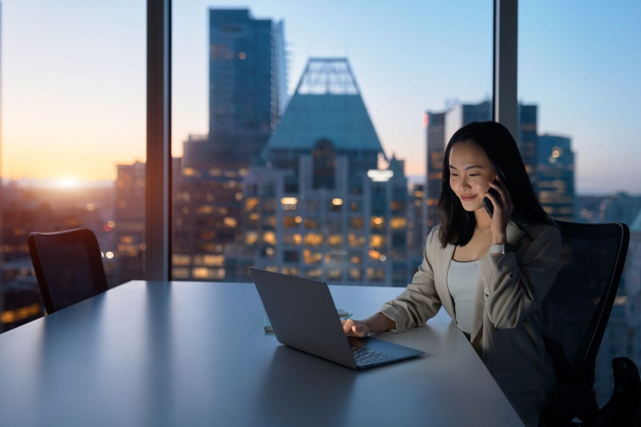 A young woman works on her laptop and talks on her phone
