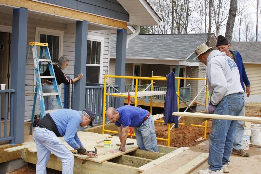 Four people are working on the construction of a wooden deck in front of a house.