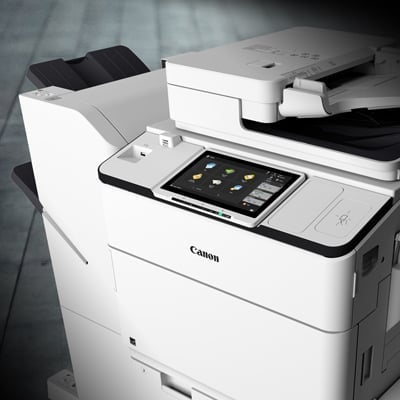 A modern Canon multifunction printer displays a touch screen interface with various application icons.